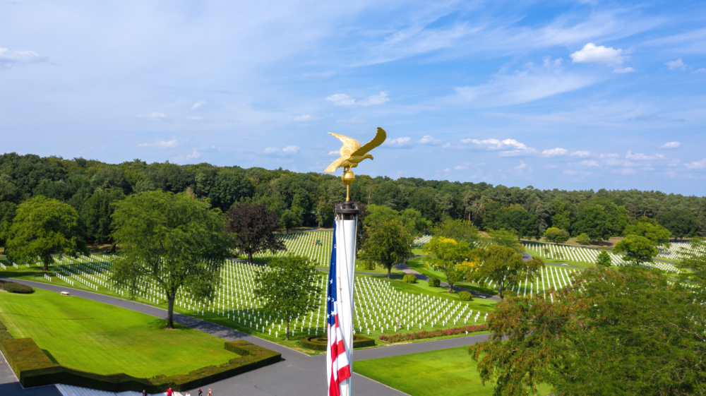 Cimetière Américain Blick auf die Spitze eines Fahnenmasts auf dem ein vergoldeter Adler sitzt, im Hintergrund ein Soldatenfriedhof
