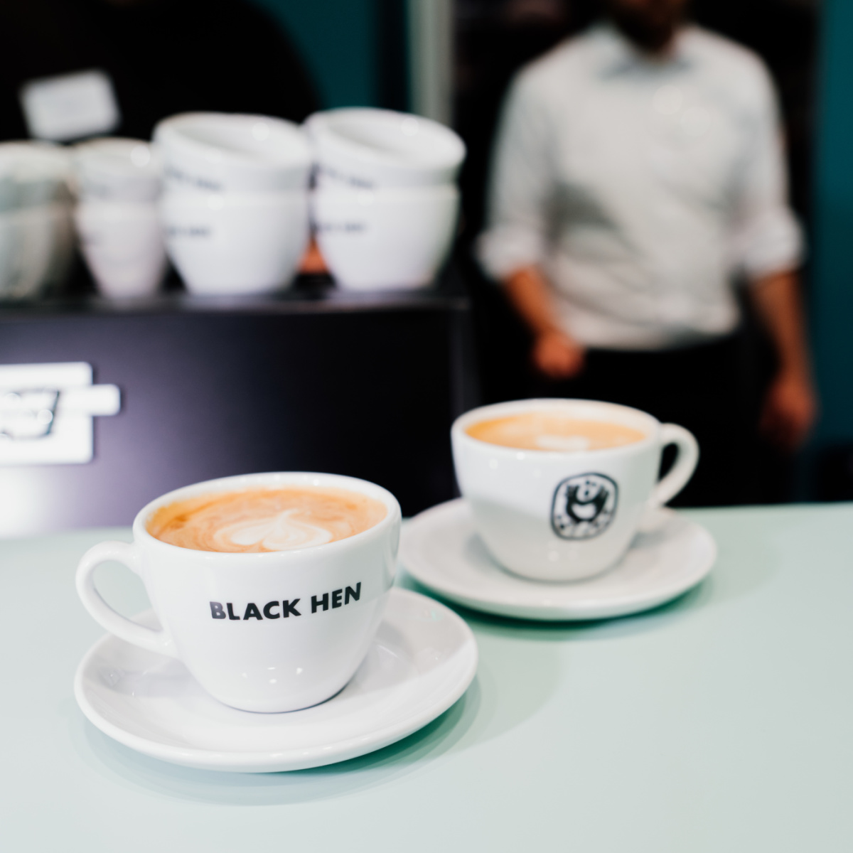 Zwei volle Kaffeetassen der Marke Black Hen stehen auf dem Tresen.